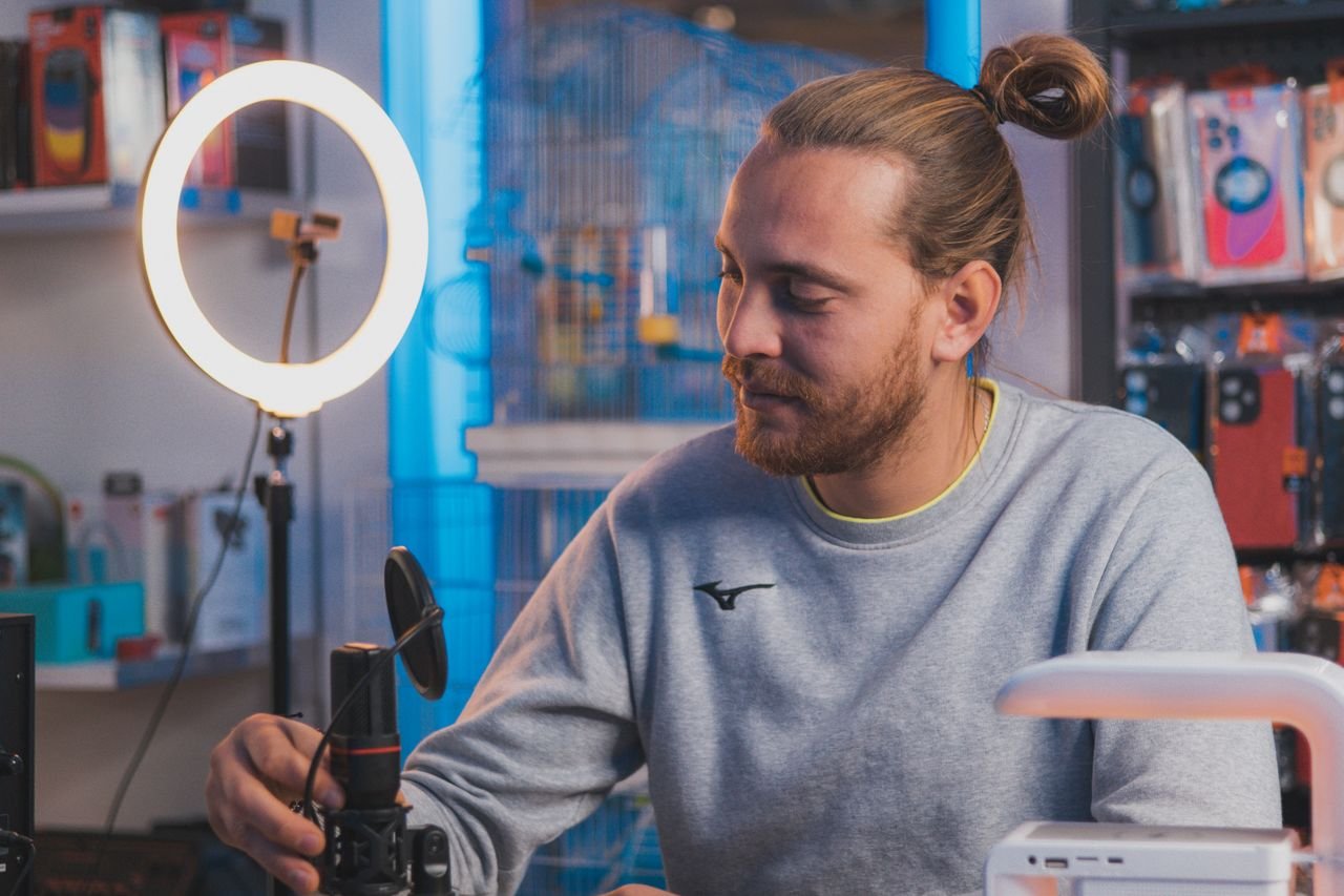Mastering the First Impression: Your intriguing post title goes here A man sitting in a studio setting adjusting a microphone with a ring light and equipment around.