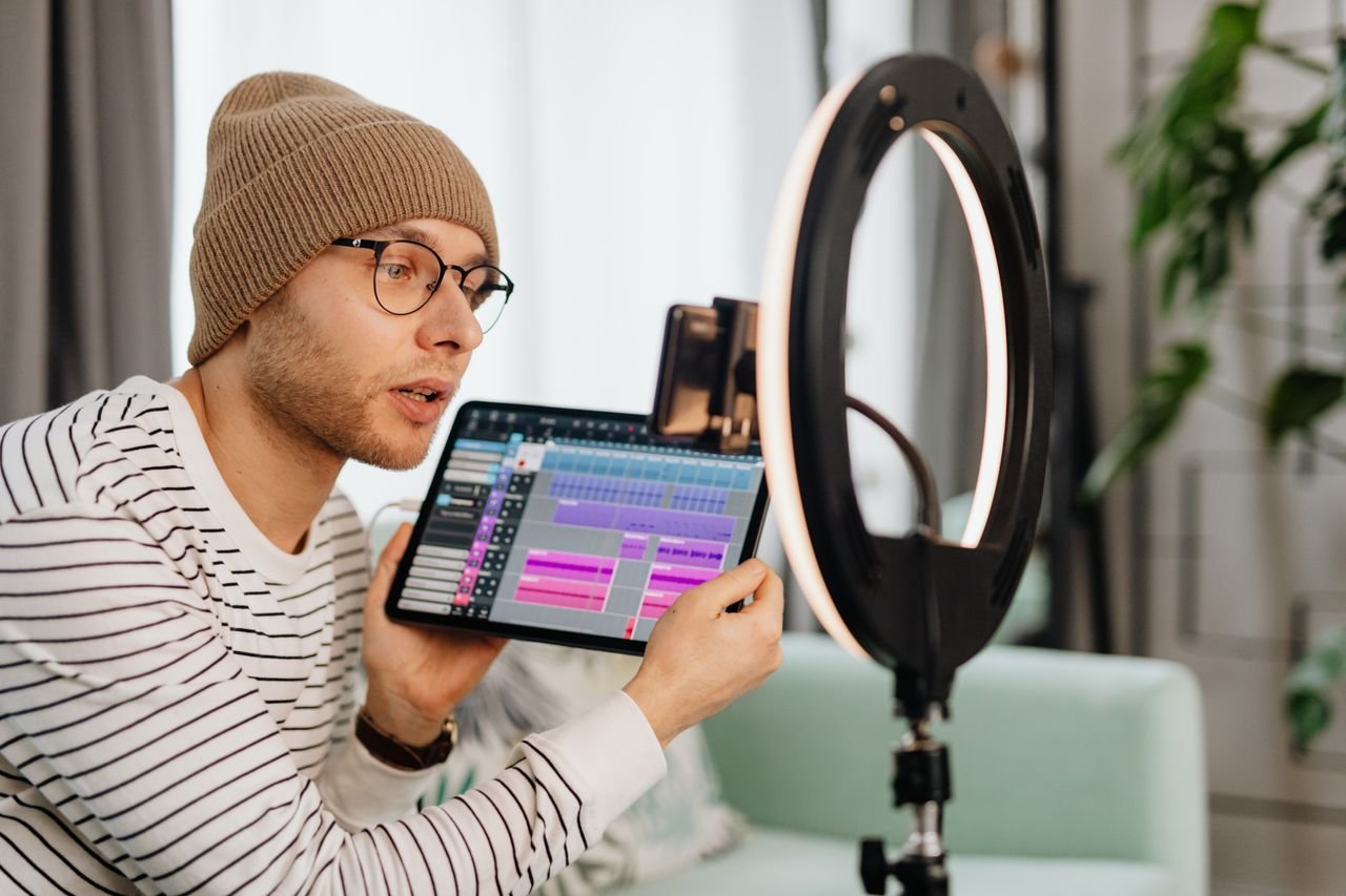 Crafting Captivating Headlines: Your awesome post title goes here A young man wearing glasses and a beanie records a video indoors using a tablet and ring light.